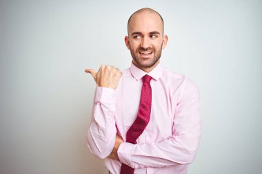 Pembe kravat takan genç bir iş adamı mutlu yüzüyle gülümseyen ve başparmağıyla yan tarafı gösteren..
