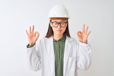 İzole edilmiş beyaz arka planda gözlük takan genç Çinli mühendis kadın rahatla ve parmaklarıyla meditasyon hareketi yaparken gözleri kapalı gülümse. Yoga konsepti.