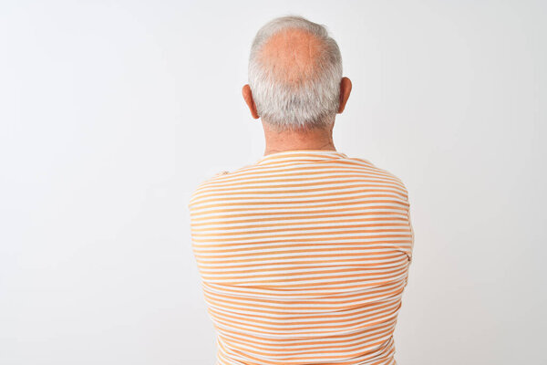 Старший седовласый мужчина в полосатой футболке стоял на изолированном белом фоне и смотрел назад со скрещенными руками.
