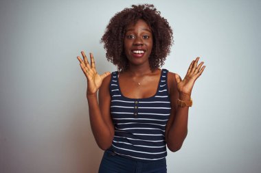 İzole edilmiş beyaz arka plan üzerinde duran çizgili tişört giyen Afrikalı genç bir kadın çılgın ve başarıyı kollarını kaldırmış ve gözleri açık bir şekilde heyecanla haykırarak kutluyor. Kazanan konsept