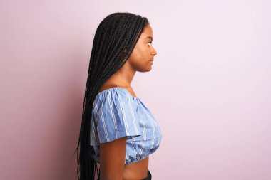 Afro-Amerikan kadın çizgili tişört giyiyor pembe arka plan üzerinde duruyor, yan yana bakıyor, rahat profil pozu veriyor kendine güveni tam bir gülümsemeyle..