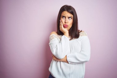 Young beautiful brunette woman over pink isolated background thinking looking tired and bored with depression problems with crossed arms.