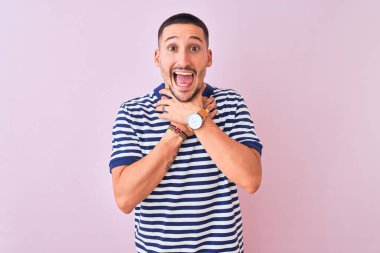 Genç yakışıklı adam pembe izole edilmiş arka plan üzerine deniz çizgili tişört giyip bağırıyor ve boğuluyor çünkü acı verici bir boğulma. Sağlık problemi. Boğulma ve intihar konsepti.