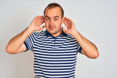 Sıradan çizgili polo giyen genç bir adam izole edilmiş beyaz arka planda dikilmiş iki elini de kulak hareketlerinde, dedikoduya meraklı olarak duymaya çalışıyor. İşitme problemi, sağır