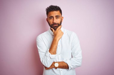 Soyutlanmış pembe arka planda duran zarif gömlekli genç Hintli işadamı çapraz kollar ve çeneyle gülümseyen kameraya kendinden emin bir şekilde bakıyor. Olumlu düşünüyorum..