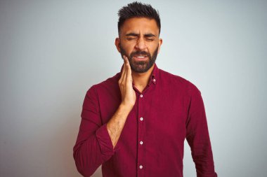 İzole edilmiş gri arka planda duran kırmızı şık gömlek giyen genç Hintli adam diş ağrısı ya da diş ağrısı yüzünden ağız ve acı dolu yüz ifadelerine dokunuyor. Dişçi konsepti.