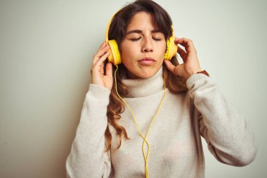 Young beautiful woman listening to music using headphones over white isolated background with serious expression on face. Simple and natural looking at the camera.