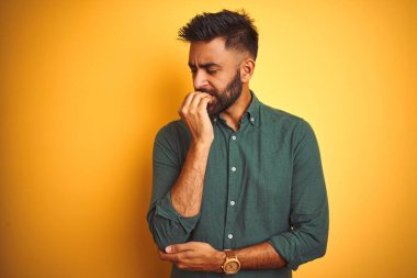 İnzivaya çekilmiş beyaz arka plan üzerinde duran zarif gömlekli genç Hintli işadamı elleri ağız yiyen tırnaklarla gergin ve stresli görünüyor. Endişe sorunu.