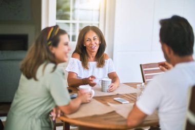 Güzel bir aile terasta oturmuş kahve içiyor, konuşuyor ve gülümsüyor.