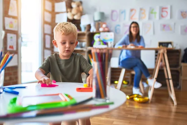 年轻的高加索孩子和老师在学校玩耍 游戏室的母亲和儿子用彩色铅笔画了一幅画 背景上的年轻女子坐在桌子上 — 图库照片