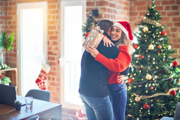 年轻漂亮的夫妇面带微笑 既快乐又自信 在家里抱着礼物 抱着圣诞树站着 — 图库照片