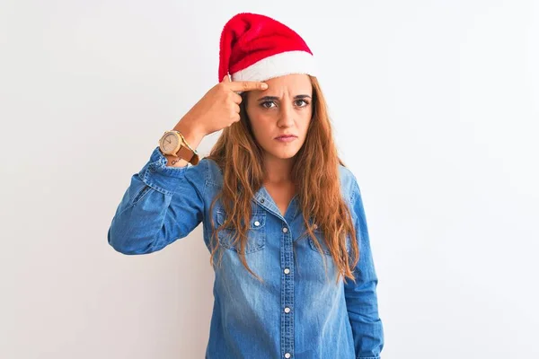 若い美しい赤毛の女性が孤立した背景の上にクリスマスの帽子をかぶって額ににきび 黒頭の醜い感染に不幸な指しています にきびと皮膚の問題 — ストック写真