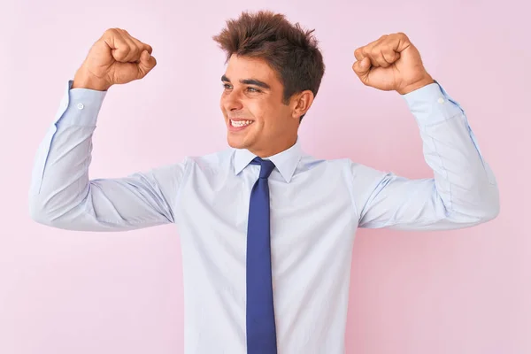 Young handsome businessman wearing shirt and tie standing over isolated pink background showing arms muscles smiling proud. Fitness concept.