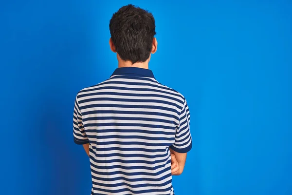 十代の男の子身に着けていますカジュアルTシャツ立っています上の青孤立した背景立ち後ろ見ます離れてとともに交差腕 — ストック写真