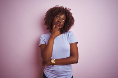 Genç Afrikalı Afro kadın pembe bir arka plan üzerinde dikilip soru soran, düşünceli bir ifade takınıyor. Düşünceli bir yüzle gülümsüyor. Şüphe kavramı.