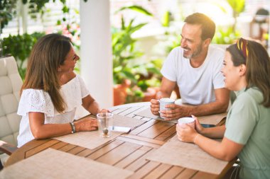 Güzel bir aile terasta oturmuş kahve içiyor, konuşuyor ve gülümsüyor.