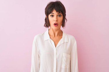 İzole edilmiş pembe arka plan üzerinde duran beyaz tişörtlü genç ve güzel bir kadın. Şaşırtıcı bir ifade, korku ve heyecanlı bir yüz ifadesiyle dehşete düşmüş ve şok olmuştu..