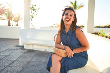 Genç, güzel bir kadın mutlu bir şekilde gülümsüyor. Güneşli bir yaz gününde Tenerife, Puerto de la Cruz 'da bir bankta oturuyor.