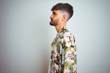 Tatilde dövmeli bir adam yaz gömleği giyiyor. İzole edilmiş beyaz arka plan üzerinde duruyor. Yan tarafa bakıyor..