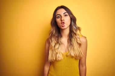Young beautiful woman wearing t-shirt over yellow isolated background making fish face with lips, crazy and comical gesture. Funny expression.
