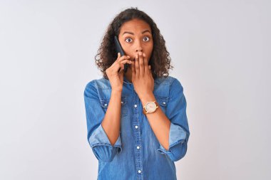 Akıllı telefondan konuşan genç Brezilyalı bir kadın izole edilmiş beyaz arka planda duruyor. Ağzını kapatıyor. Utancından ağzı açık kalmış, korkunun ifadesi, sessizlikten korkmak, gizli konsept.