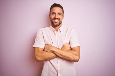 Pembe izole edilmiş arka plan üzerinde zarif bir tişört giyen genç yakışıklı kollarını kavuşturup kameraya bakan mutlu bir yüz. Pozitif kişi.