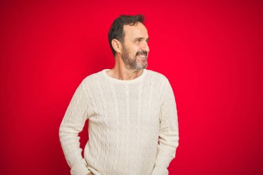 Yakışıklı, orta yaşlı, gri saçlı, soyutlanmış kırmızı arka planda, yüzünde gülümsemeyle, doğal bir ifadeyle yan yana duran yaşlı bir adam. Kendinden emin gülen.