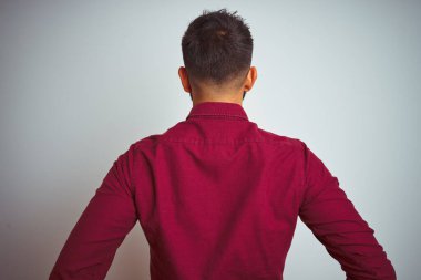 Kırmızı şık gömlekli genç Hintli adam izole edilmiş gri arka planda dikiliyor geriye bakıyor kolları vücudunda.