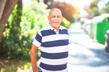 Kıdemli yakışıklı adam mutlu ve kendinden emin gülümsüyor. Kasaba caddesinde yüzünde gülümsemeyle dikilirken