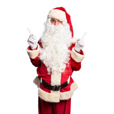 Orta yaşlı yakışıklı adam, Noel Baba kostümü ve sakal takmış, gülümseyerek farklı yönleri işaret ediyor. Reklam için boşluk kopyala