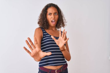 İzole edilmiş beyaz arka plan üzerinde duran çizgili tişört giyen genç Brezilyalı kadın korku ifadesinden korkuyor ve dehşete düşüyor. El hareketlerini durdur, şok içinde bağır. Panik konsepti.