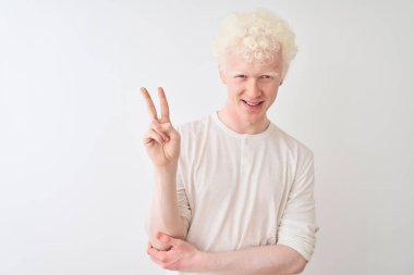Genç albino sarışın adam rahat t-shirt izole beyaz arka plan üzerinde duran giyen mutlu yüz zafer işareti yapıyor kameraya göz kırparak gülümseyerek. İki numara.