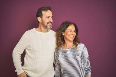 Güzel bir orta yaşlı çift, izole edilmiş mor arka plan üzerine kışlık kazak giyip yüzünde gülümsemeyle, doğal bir ifadeyle yan yana bakıyorlar. Kendinden emin gülen.