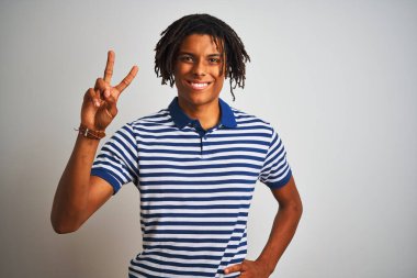 Sarı çizgili mavi polo giyen Afro adam izole edilmiş beyaz arka planda durup kameraya bakarak zafer işareti yapıyor. İki numara..