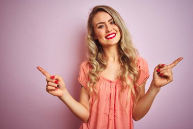 Pembe izole edilmiş arka plan üzerinde duran tişört giyen genç ve güzel bir kadın farklı yönleri gösteren kendine güveniyle gülümsüyor. Reklam için boşluk kopyala