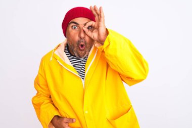 Yağmurluk giyen ve yünlü şapkalı orta yaşlı bir adam izole edilmiş beyaz arka planda dikiliyor. Şaşırmış yüz ifadesiyle şaşırmış, parmaklarından bakan gözler. İnançsız ifade.