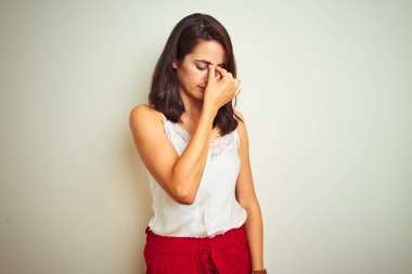 İzole edilmiş beyaz arka plan üzerinde duran tişört giyen genç ve güzel bir kadın yorgun burnu ve gözleri ovuşturarak yorgunluk ve baş ağrısı hissediyor. Stres ve hüsran kavramı.