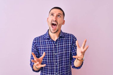 Soyutlanmış arka planda duran yakışıklı genç adam kızgın ve çılgın bir şekilde bağırıyor ve agresif bir ifade ve kollarla bağırıyor. Hayal kırıklığı konsepti.