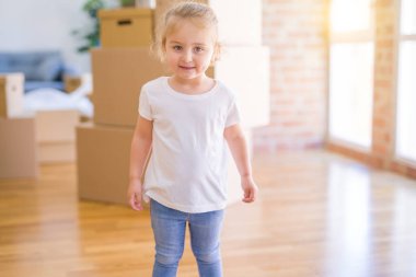 Güzel aile, anne-babalar kanepede kahve içme oturmuş karton kutular etrafında yeni evde oynayan çocuğuna bakıyor