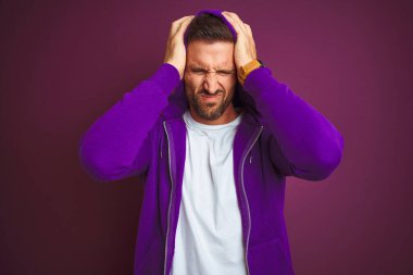 Spor tişörtü giyen genç fitness adamı ve mor izole edilmiş arka plan üzerine kapüşon giymiş. Ağrı ve migren yüzünden çaresiz ve stresli. Ellerini başının üstüne koy..