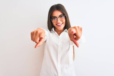 Gözlüklü genç ve güzel bir iş kadını izole edilmiş beyaz arka planda duruyor. Sana ve kameraya parmaklarıyla bakıyor.