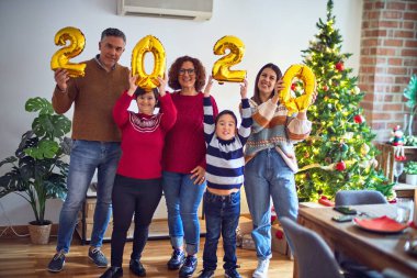 Mutlu ve kendinden emin gülümseyen güzel bir aile. Ayakta durup poz vermek 2020 balonu evde Noel ağacı etrafında kutluyor.