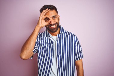 Genç, yakışıklı Hintli, yaz çizgili gömlekli, pembe arka planda. Tamam, el hareketleriyle gülümsüyor, gözleriyle mutlu yüzlere bakıyor..