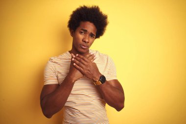 Afro saçlı, çizgili tişörtlü, izole edilmiş sarı arka plan üzerinde duran Amerikalı bir adam. Ellerinde ve parmaklarında ağrı var. Eklem iltihabı.