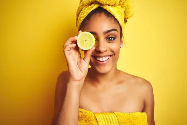 シャワーの後にタオルを着たアフロの女性は 歯を見せる自信のある笑顔で立ち上がり 笑顔で孤立した黄色の背景の上にスライスレモンを保持 — ストック写真