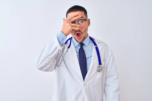 年轻的医生 戴着听诊器 用手捂住脸和眼睛 在孤立的背景下窥视 尴尬地看着手指 — 图库照片