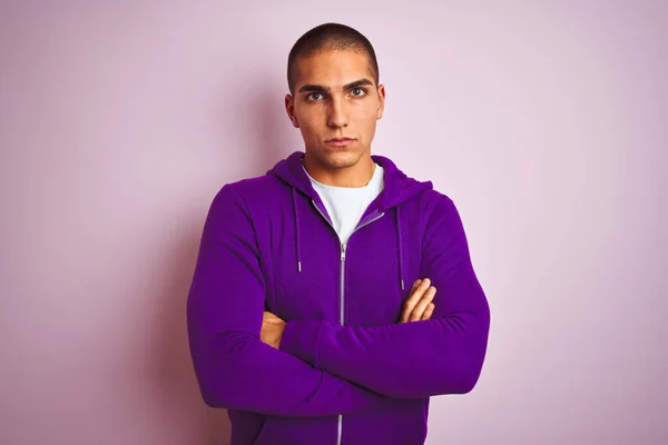 ピンクの隔絶された背景に紫のスウェットシャツを着た若いハンサムな男は懐疑的で緊張し 両腕を組んで顔に不承認の表現 負の人 — ストック写真