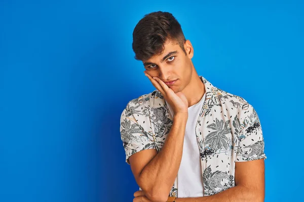 Young indian man on vacation wearing hawiaian shirt standing over isolated blue background thinking looking tired and bored with depression problems with crossed arms.