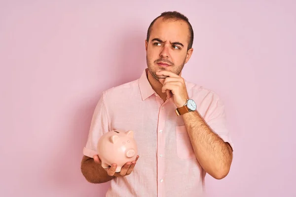 Jovem Segurando Piggybank Sobre Fundo Rosa Isolado Rosto Sério Pensando — Fotografia de Stock