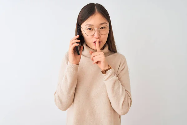 年轻的中国女人在智能手机上通过孤立的白色背景说话 要求保持安静 手指放在嘴唇上 沉默和秘密概念 — 图库照片